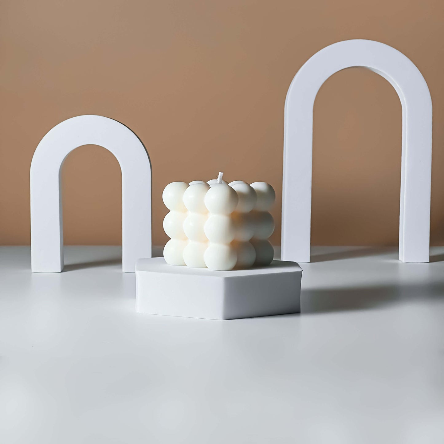 White candle with a bubble-like texture on a gray surface with a beige background