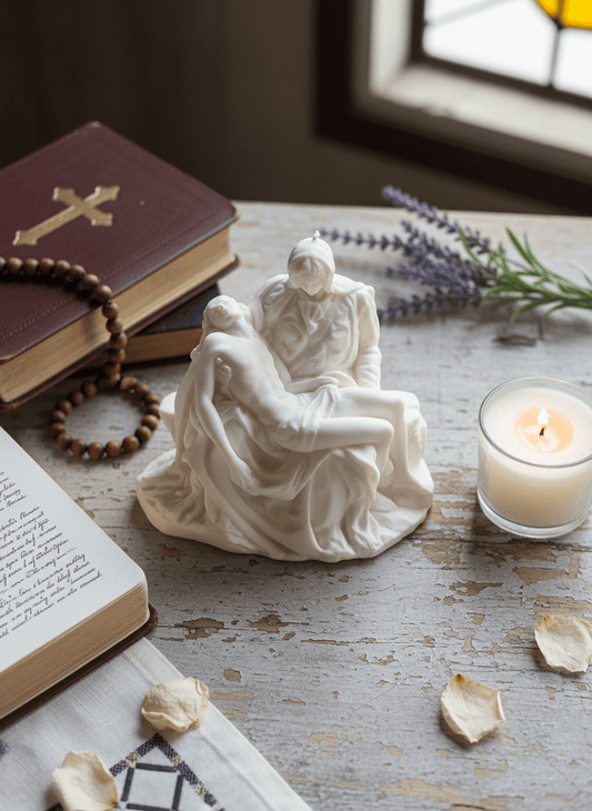 Statue of the Pieta on a wooden surface with a candle, book, and rosary.