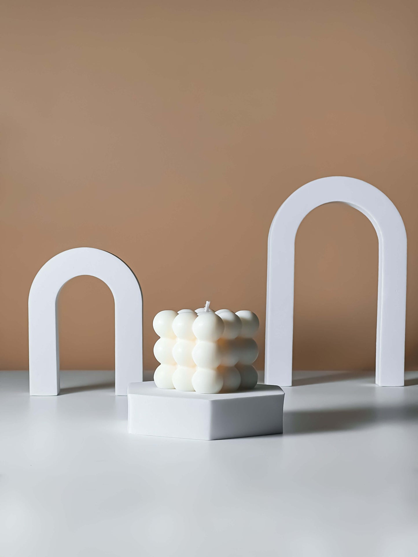 White candle with a bubble-like texture on a gray surface with a beige background